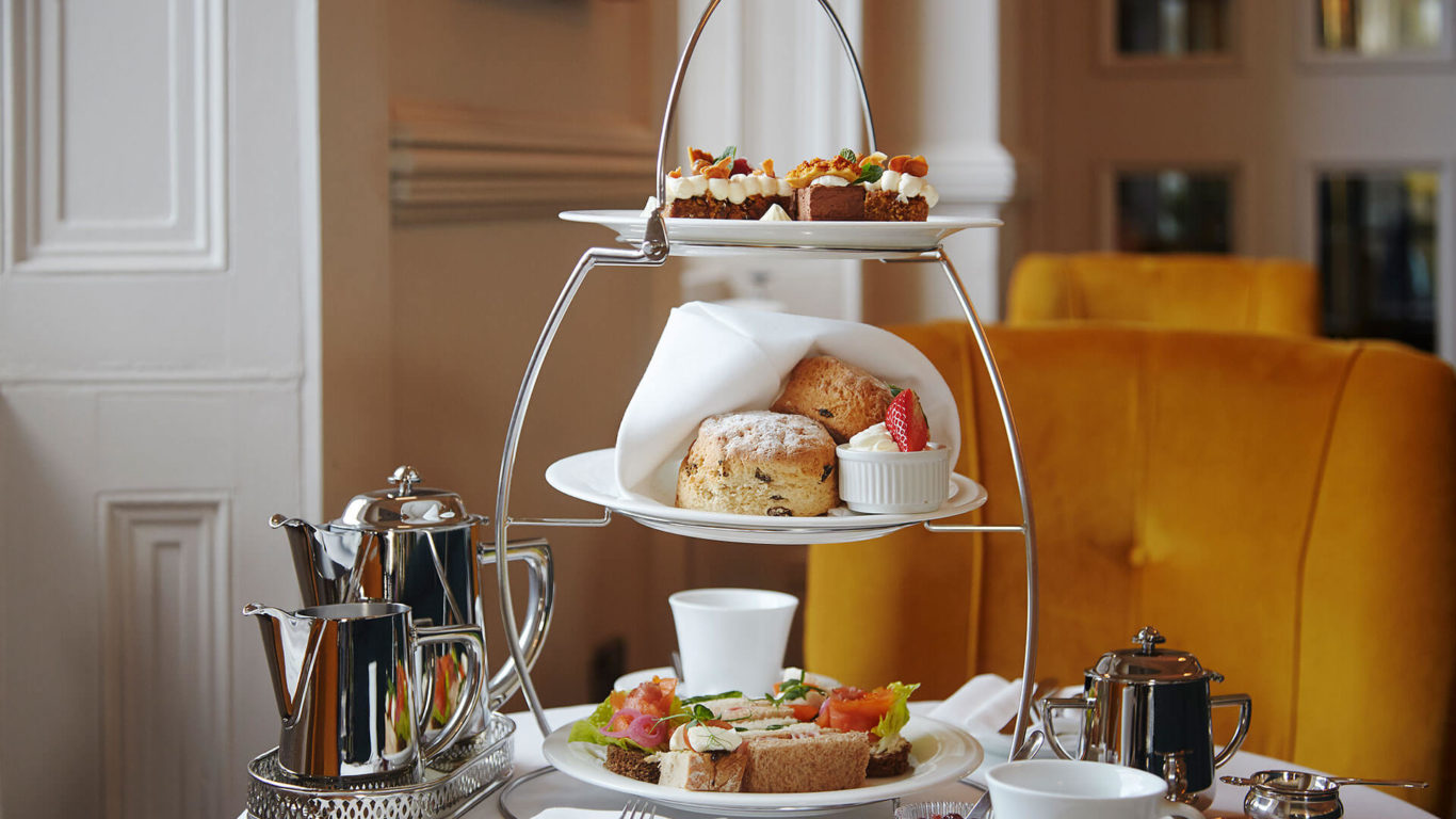 Elegant afternoon tea with scones, desserts, and sandwiches in a luxurious hotel lounge with plush yellow seating.