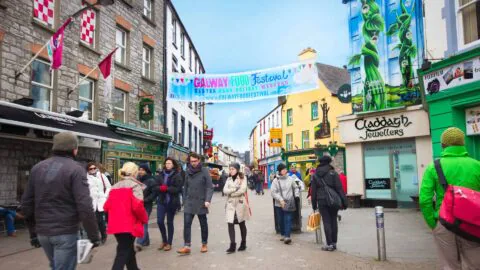 Bustling Galway street scene with colourful shops and festival banner, offering vibrant local culture and dining experiences.