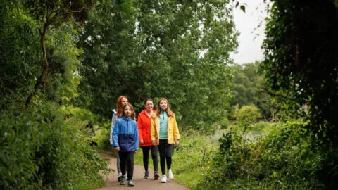 Happy family strolling on lush green path surrounded by trees, enjoying a peaceful nature walk near the hotel.