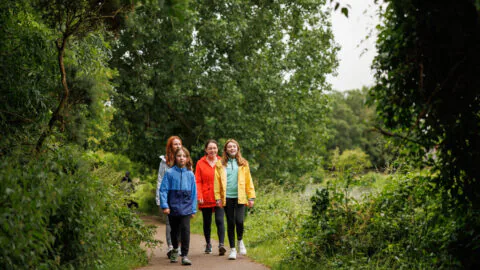 Happy family strolling on lush green path surrounded by trees, enjoying a peaceful nature walk near the hotel.