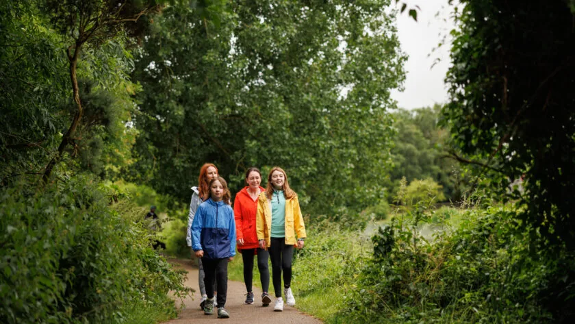 Happy family strolling on lush green path surrounded by trees, enjoying a peaceful nature walk near the hotel.