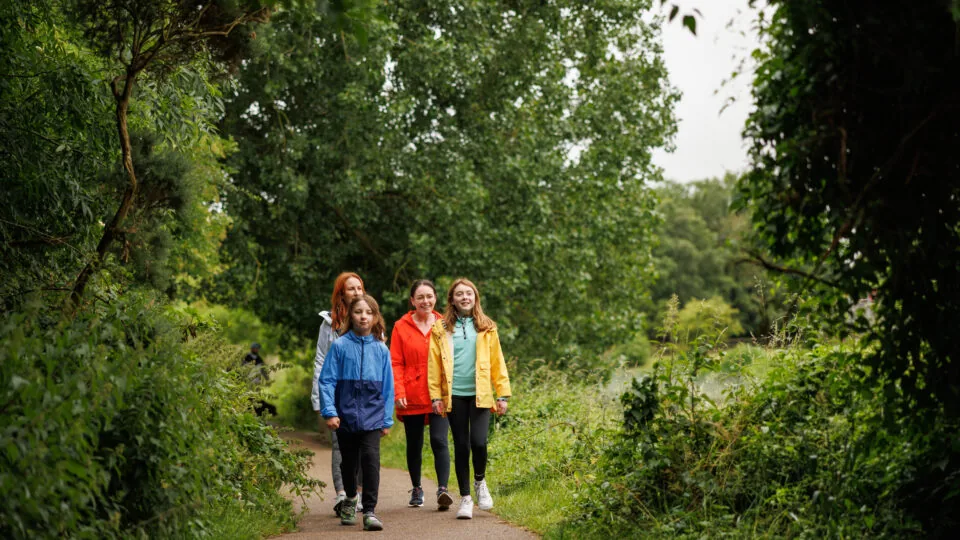 Happy family strolling on lush green path surrounded by trees, enjoying a peaceful nature walk near the hotel.