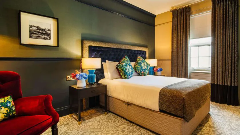 Elegant hotel room with cosy double bed, vibrant cushions, luxurious decor, and a warm atmosphere with natural light.