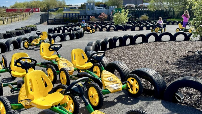 Guests enjoy outdoor fun on yellow pedal karts around a tyre track under a clear blue sky at the hotel playground.