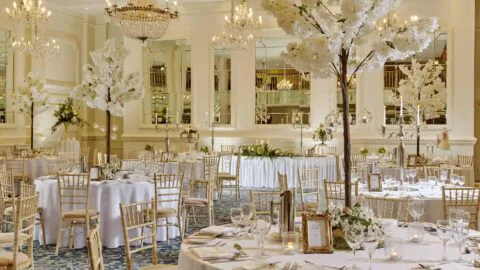 Elegant hotel ballroom with chandeliers, round tables, gold chairs, floral centrepieces, perfect for weddings or events.
