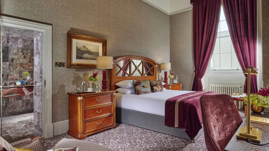 Elegant hotel room with plush bedding, luxurious drapes, and stylish furnishings, offering comfort and charm.
