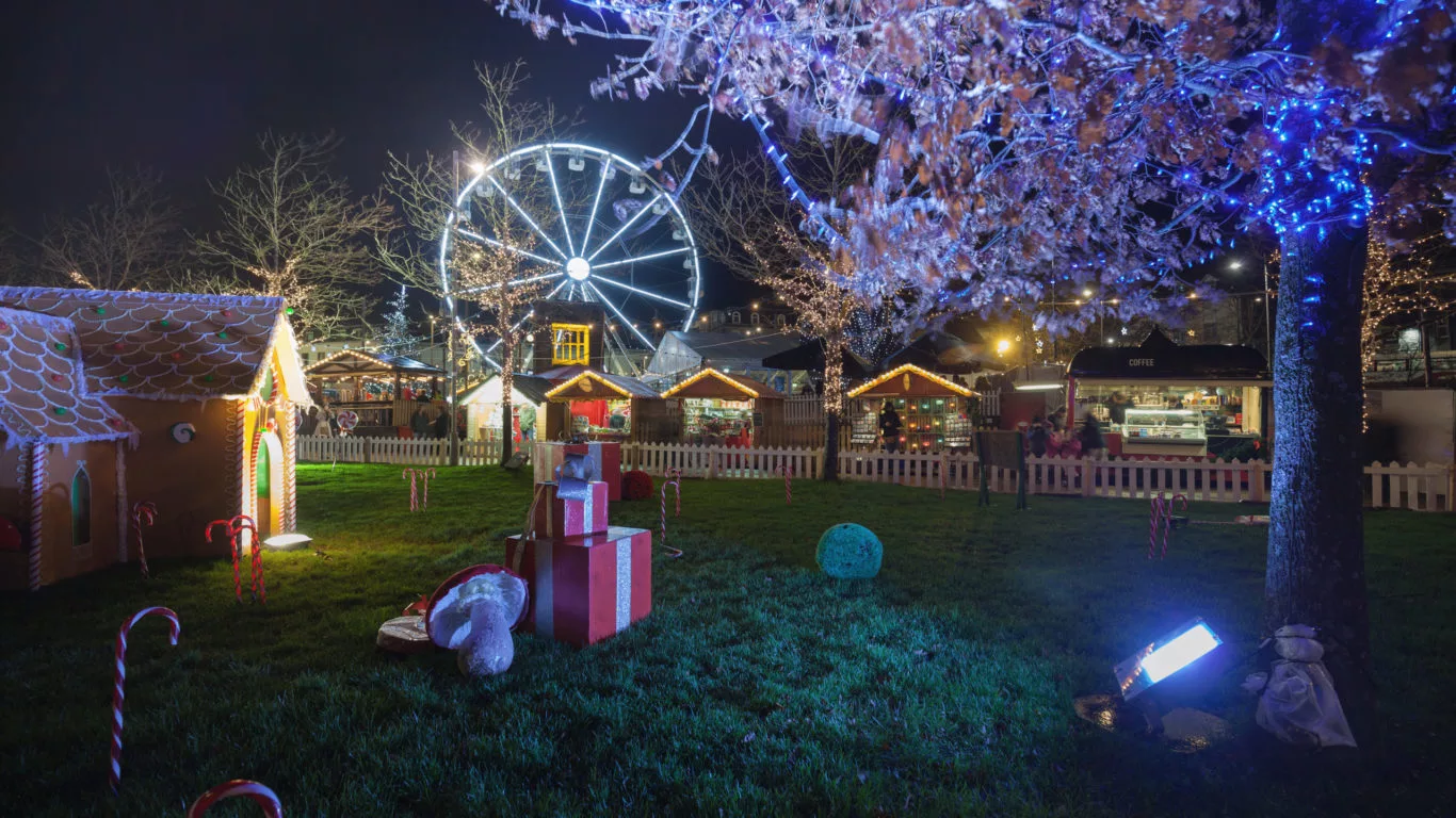 Enchanting night garden with festive lights, gingerbread house, Ferris wheel, and cosy market stalls for a magical stay.