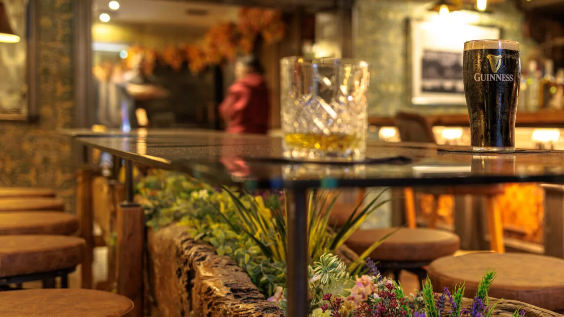 Warm hotel bar with wooden stools, floral decor, and pints of Guinness, inviting ambiance for relaxation and socialising.