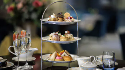 Elegant afternoon tea with cakes and sandwiches, served with sparkling wine in a luxurious hotel setting.