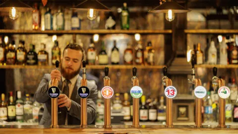 Bartender serving at stylish hotel bar with warm lighting, showcasing an extensive range of beers on tap and spirits.