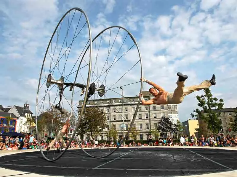 Guests enjoy an outdoor acrobat show with vibrant entertainment near a charming hotel backdrop and lively community vibe.