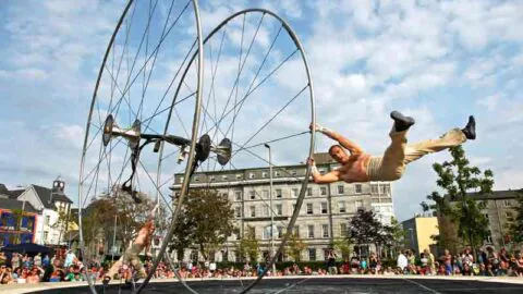 Guests enjoy an outdoor acrobat show with vibrant entertainment near a charming hotel backdrop and lively community vibe.