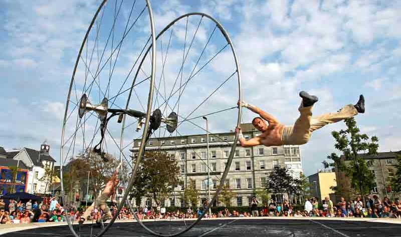 Guests enjoy an outdoor acrobat show with vibrant entertainment near a charming hotel backdrop and lively community vibe.