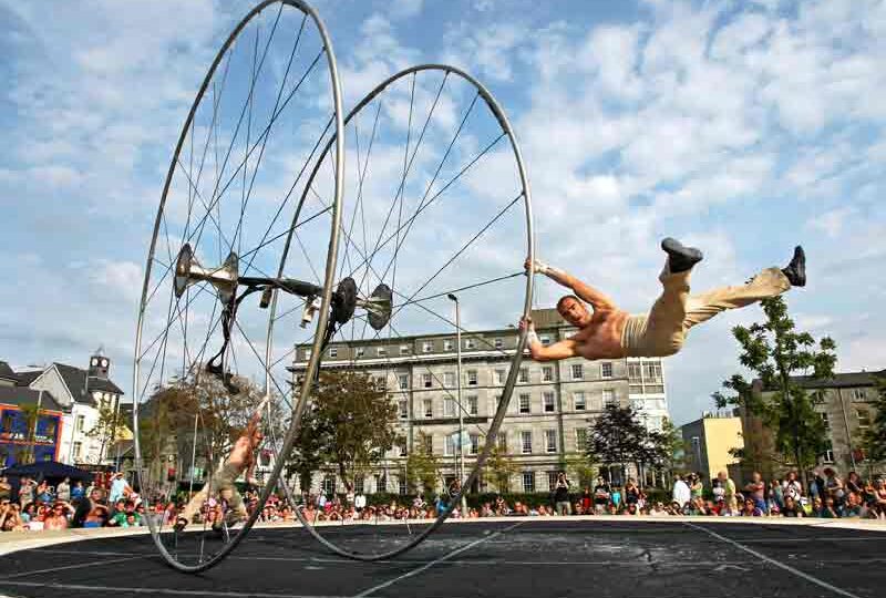 Guests enjoy an outdoor acrobat show with vibrant entertainment near a charming hotel backdrop and lively community vibe.