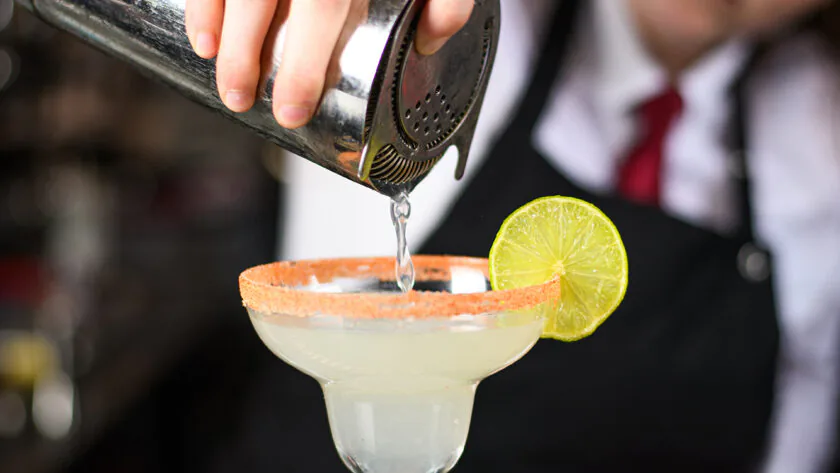 Bartender pours cocktail into margarita glass with lime, creating a vibrant hotel bar experience.