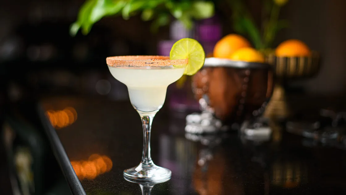 Enjoy a refreshing margarita on our elegant bar counter, with vibrant décor and a slice of lime, perfect for relaxation.