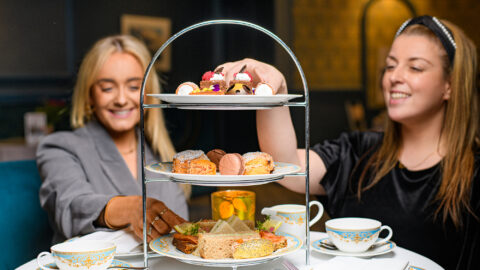 Guests enjoying elegant afternoon tea with fresh pastries, sandwiches, and fine china in a cosy hotel setting.