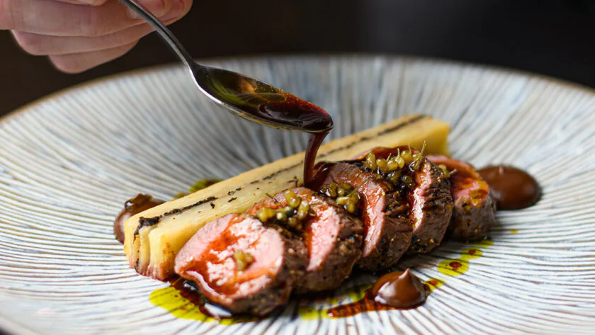 Gourmet lamb dish with rich sauce drizzle, served on elegant patterned plate, showcasing fine dining experience.