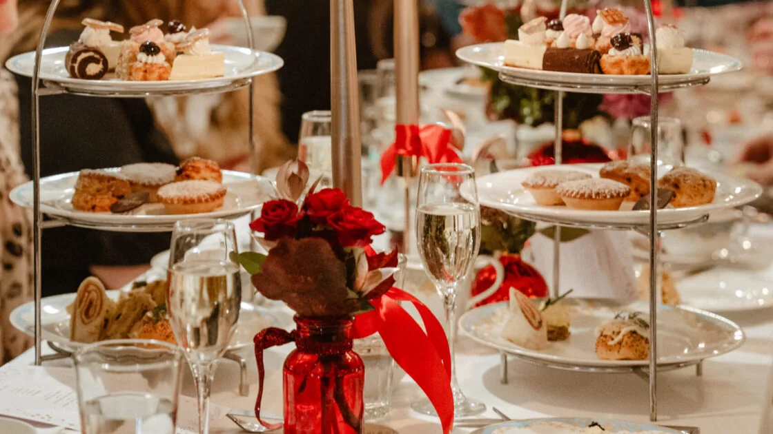 Elegant afternoon tea setting with tiered cakes, candles, and champagne at a festive hotel dining room.