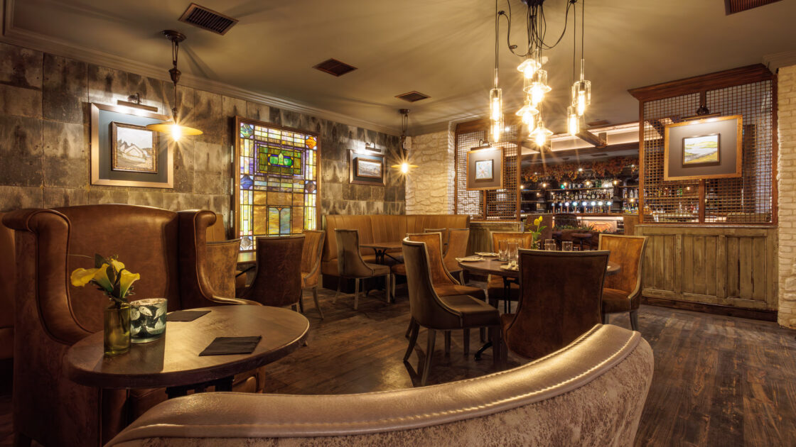 Cosy hotel lounge with leather chairs, stained glass window, soft lighting, and a fully stocked bar for a relaxing stay.