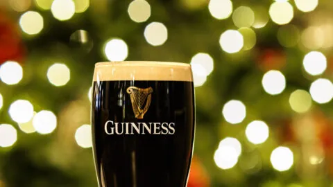 Pint of Guinness on a wooden table with warm bokeh lights in holiday setting at elegant hotel lounge.