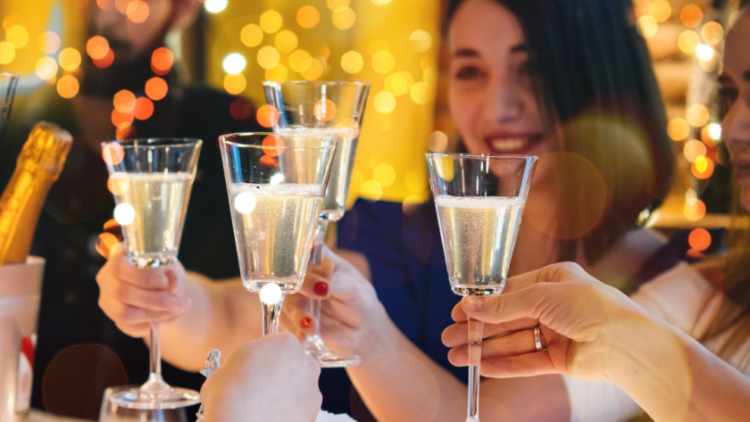 Guests toast with champagne in a warmly-lit restaurant, surrounded by festive decorations and elegant table settings.