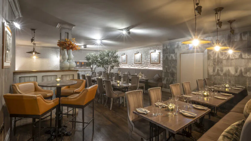 Cosy hotel dining room with elegant decor, brown leather chairs, soft lighting, candles, and wall art creating a warm ambience.