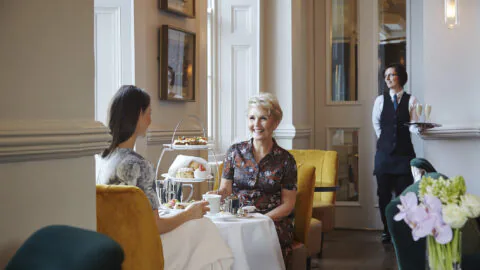 Guests enjoy afternoon tea with floral d&eacute;cor and elegant seating in a cosy hotel lounge.