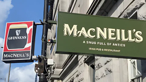 Two signs on a building: one advertising Guinness at MacNeill&rsquo;s, the other a green sign reading 