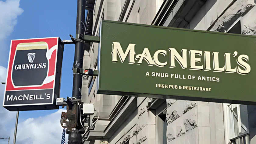 Two signs on a building: one advertising Guinness at MacNeill’s, the other a green sign reading