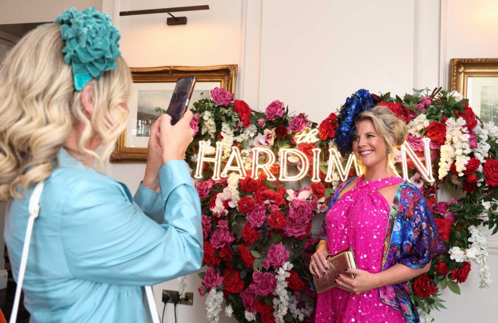 A woman in a pink dress poses for a photo in front of a floral backdrop and neon 