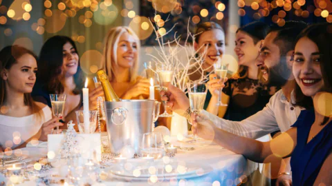 Guests enjoy a festive dinner with champagne in an elegantly decorated hotel dining room, surrounded by warm lights.