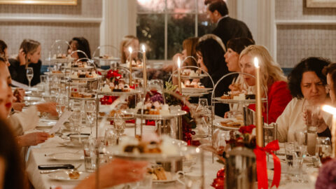 Elegant dining room with guests enjoying afternoon tea, featuring tiered trays of pastries and ambient lighting.