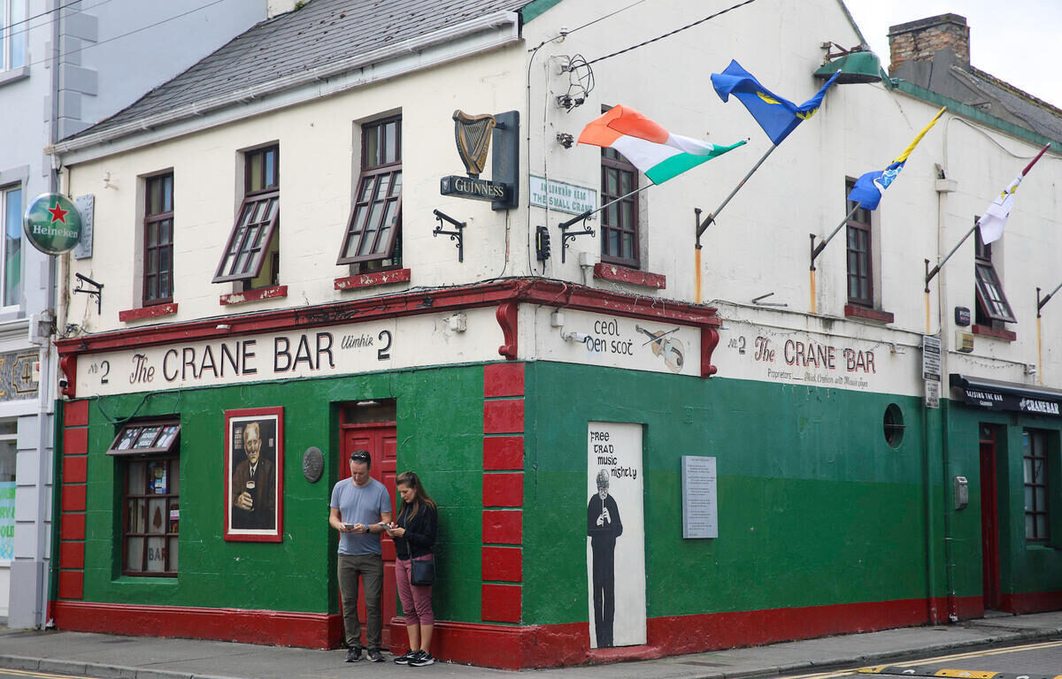 Traditional Irish pub with colourful facade, flags, and live music sign; welcoming ambiance in Galway city centre.