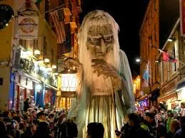 Enchanting street festival with giant puppet surrounded by lively crowds and vibrant city lights at night.
