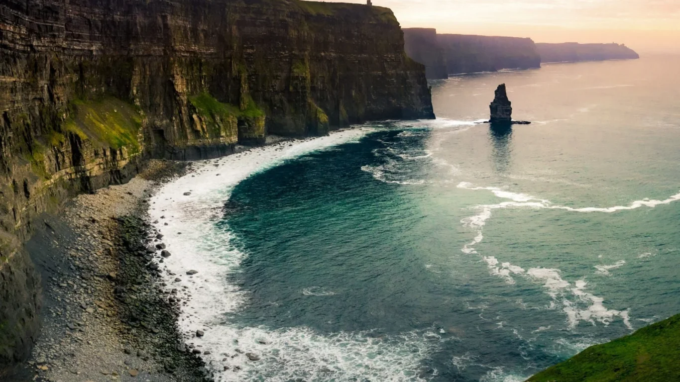 Magnificent view of the Cliffs of Moher at sunset, with lush green cliffs and the vast Atlantic Ocean, perfect for nature lovers.