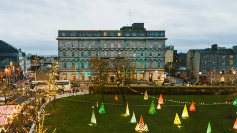 Historic hotel with festive lights, charming city views, and vibrant cone sculptures in verdant garden, ideal for travellers.