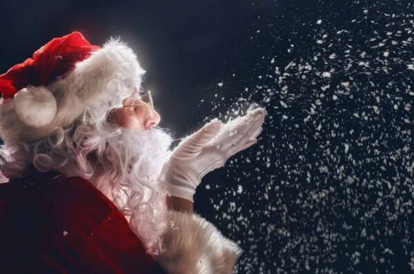Santa in festive attire blowing snowflakes, offering a magical Christmas experience at our hotel with holiday decorations.
