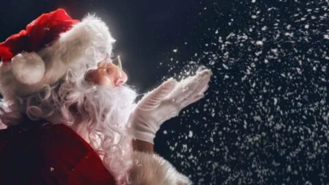 Santa in festive attire blowing snowflakes, offering a magical Christmas experience at our hotel with holiday decorations.